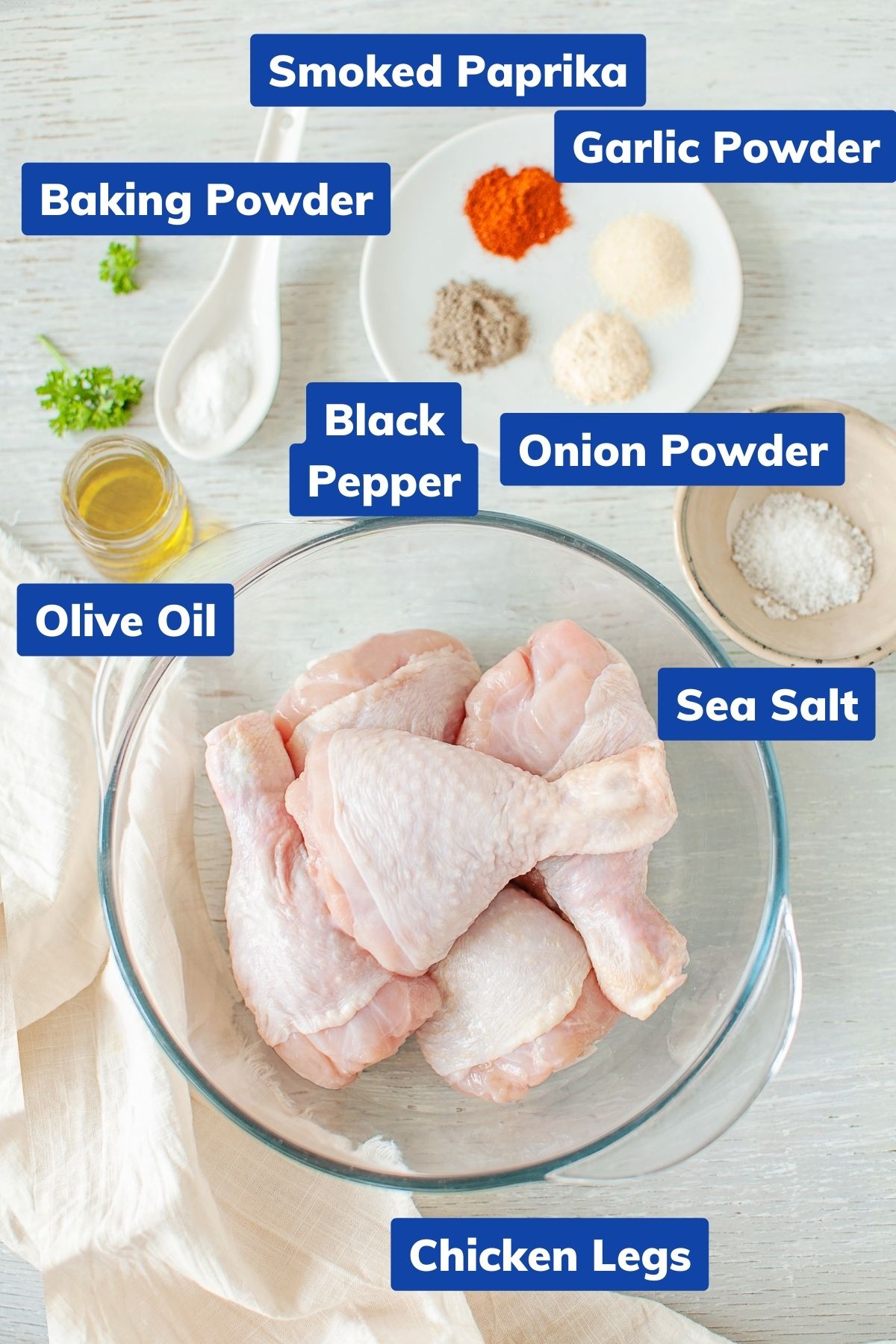 ingredients needed for air fryer fried chicken legs: smoked paprika, garlic powder, baking powder, black pepper, olive oil, sea salt, and chicken legs in separate bowls and dishes
