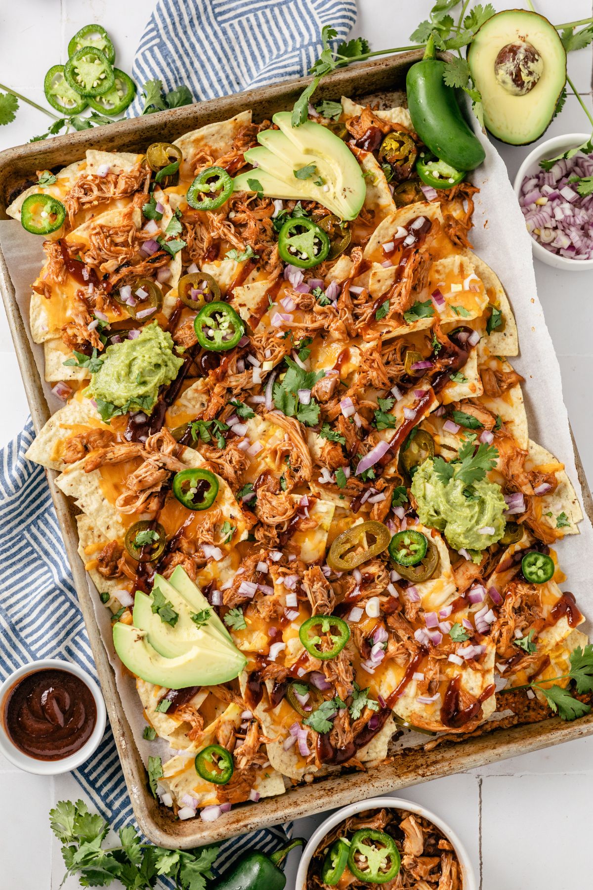 flavorful BBQ Chicken Nachos on a rectangle dish with red onions, cheese, jalapeños, avocado, guacamole, and bbq sauce