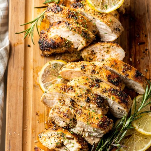 Cast Iron Chicken Breasts placed on a wooden board and topped with slices of lemon