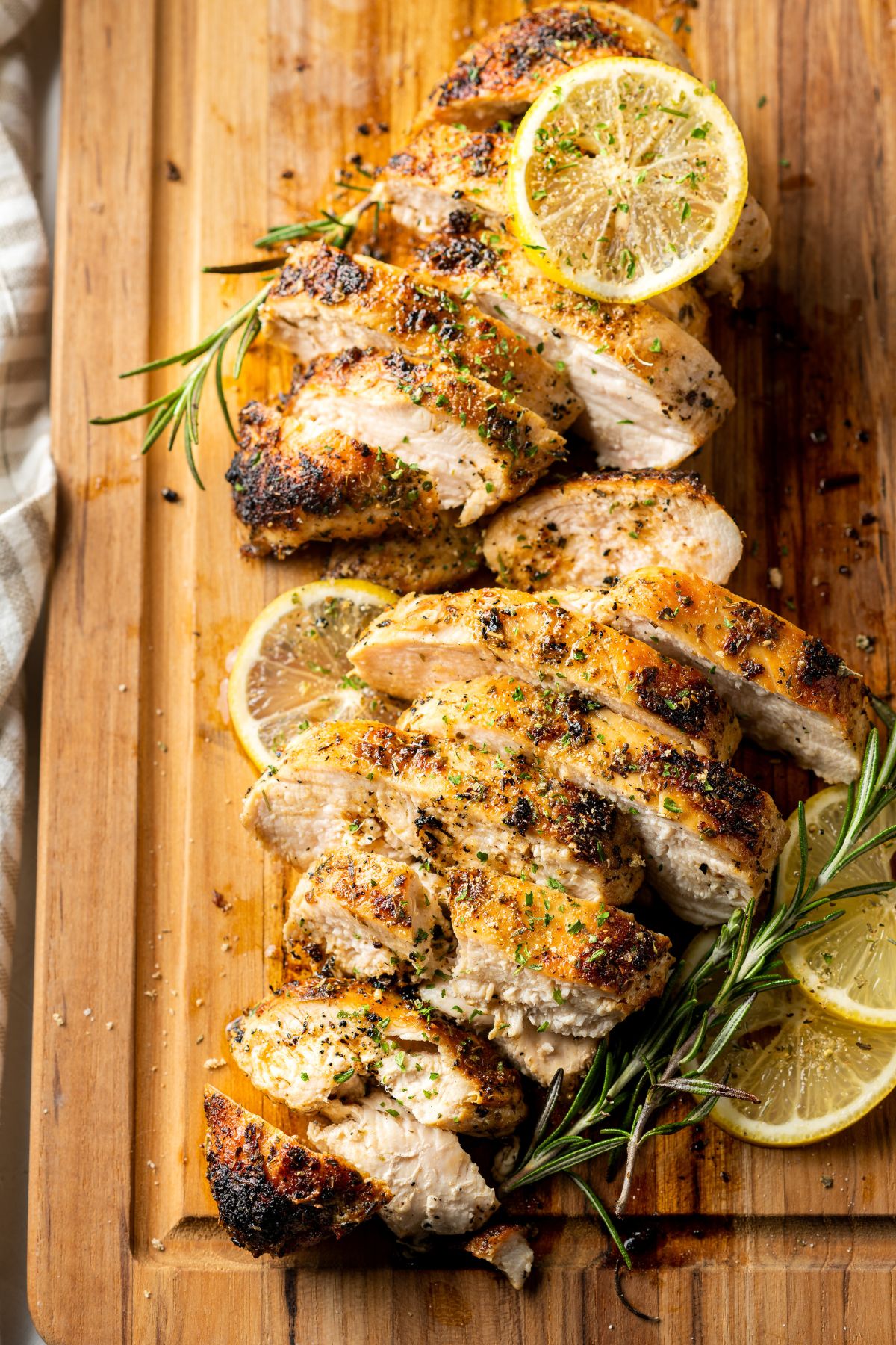 Cast Iron Chicken Breasts placed on a wooden board and topped with slices of lemon