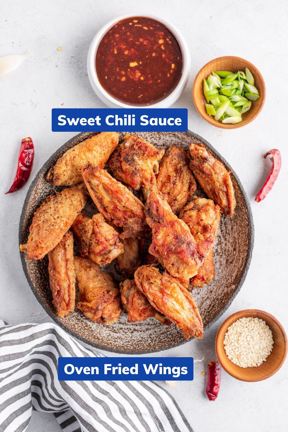 oven fried chicken wings on a large plate, sweet chili sauce, sesame seeds and chili in separate small bowls