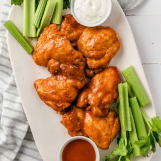 Buffalo Chicken Thighs with mayo dip and celery on a plate
