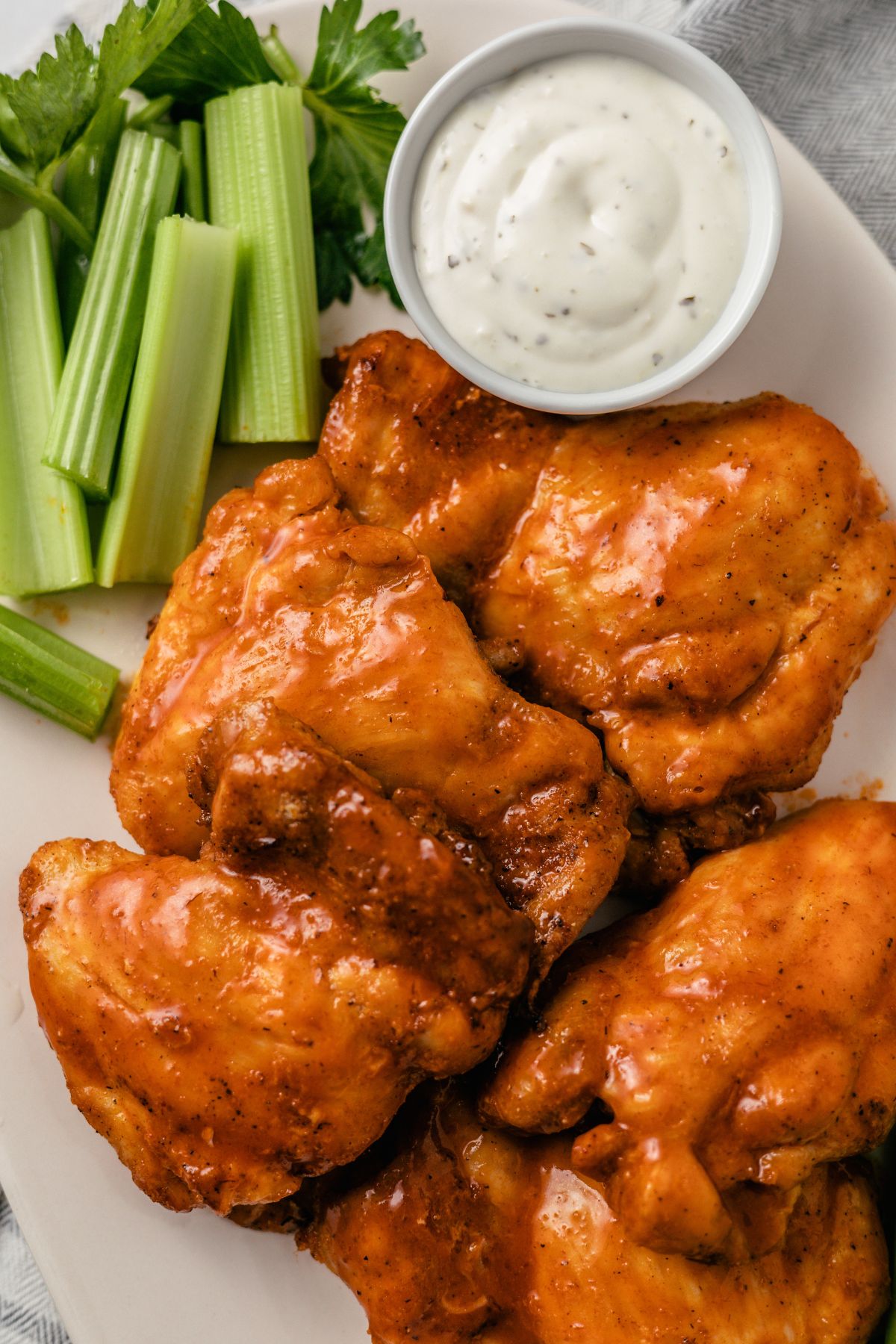 Buffalo Chicken Thighs on a plate with Frank's red hot sauce, ranch dressing, and celery sticks