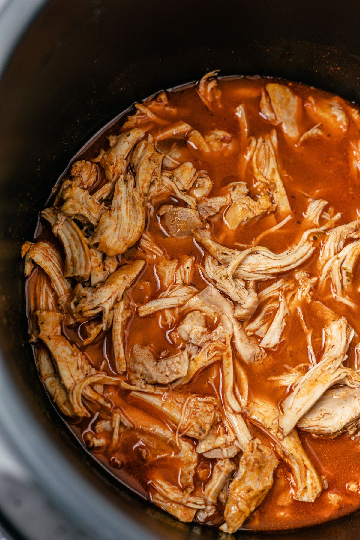 mixing shredded chicken with ranch seasoning, smoked paprika, hot sauce, and broth in a cooking pot