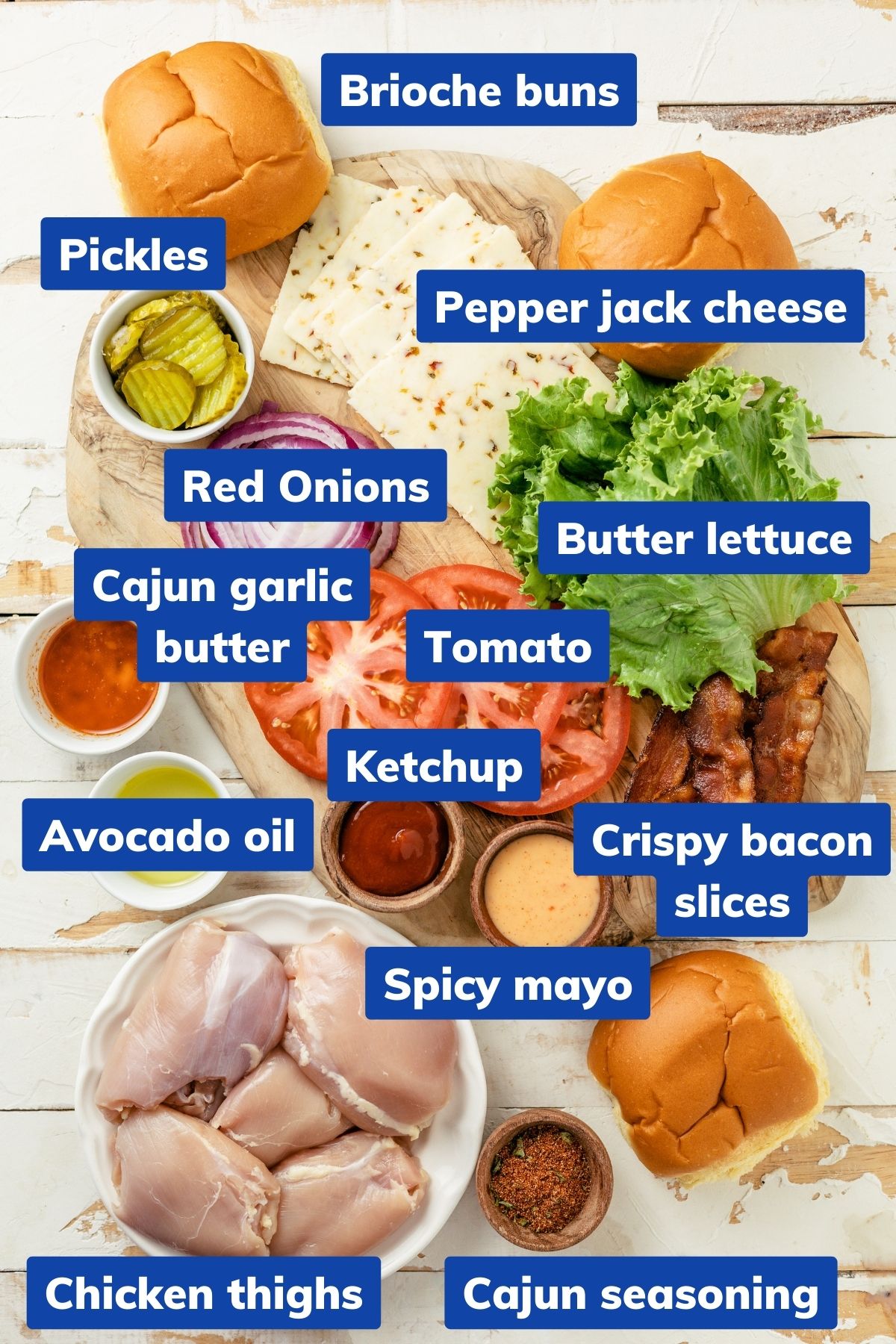 Chicken thighs, Cajun seasoning, Avocado oil, Cajun Garlic Butter, Brioche Buns, Pepper Jack Cheese, Butter Lettuce, Tomato, Pickles, Red Onions, Ketchup, Crispy Bacon Slices, Spicy Mayo placed on separate bowls and a wooden board