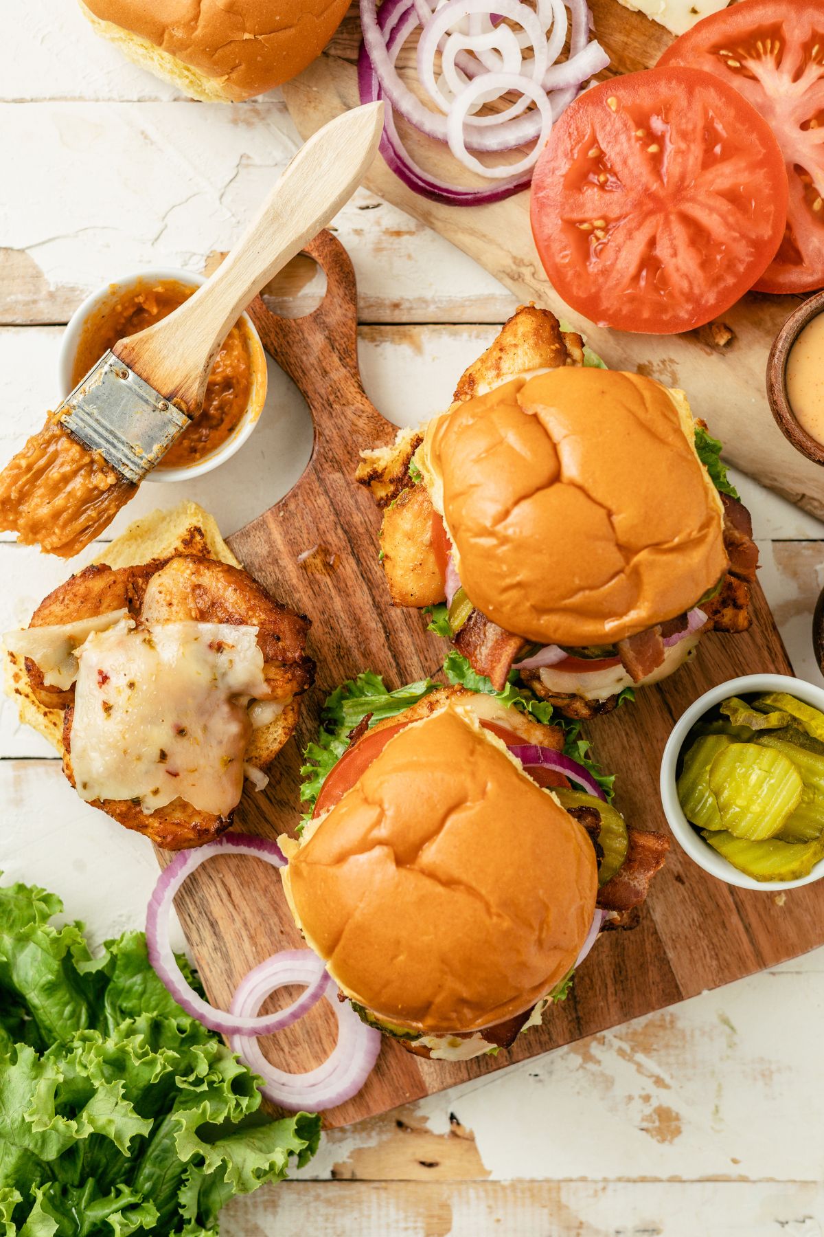 juicy Cajun Chicken Burgers on a wooden board surrounded by different burger toppings