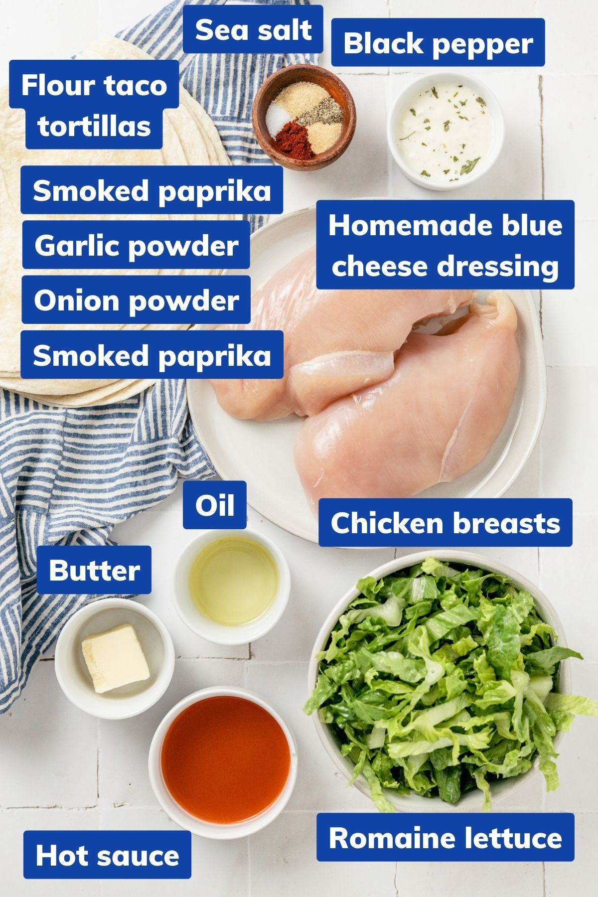 Chicken breasts, optional sea salt, black pepper, smoked paprika, garlic and onion powders, oil, buffalo and Frank's red hot sauces, unsalted butter, tortillas (flour or corn), romaine lettuce, blue cheese dressing, and avocado or olive oil spray are displayed in separate bowls.