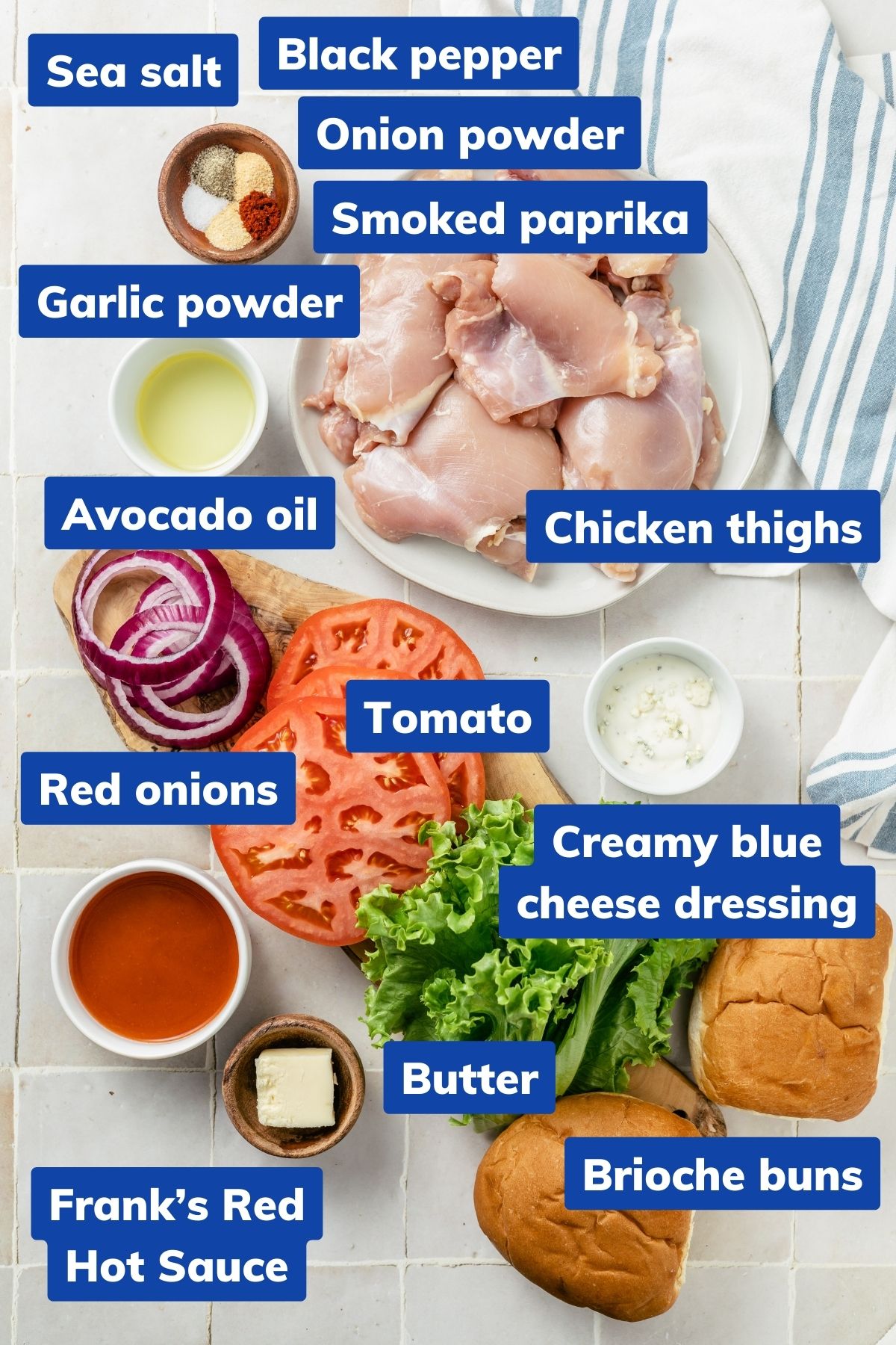 ingredients for buffalo chicken sandwiches are displayed in individual bowls, including boneless skinless chicken thighs, seasonings like sea salt, black pepper, smoked paprika, garlic and onion powder, and avocado oil. Additionally, there's Frank's Red Hot Sauce, melted butter, soft brioche buns, fresh produce like butter lettuce, tomatoes, red onions, and a bowl of creamy blue cheese dressing.