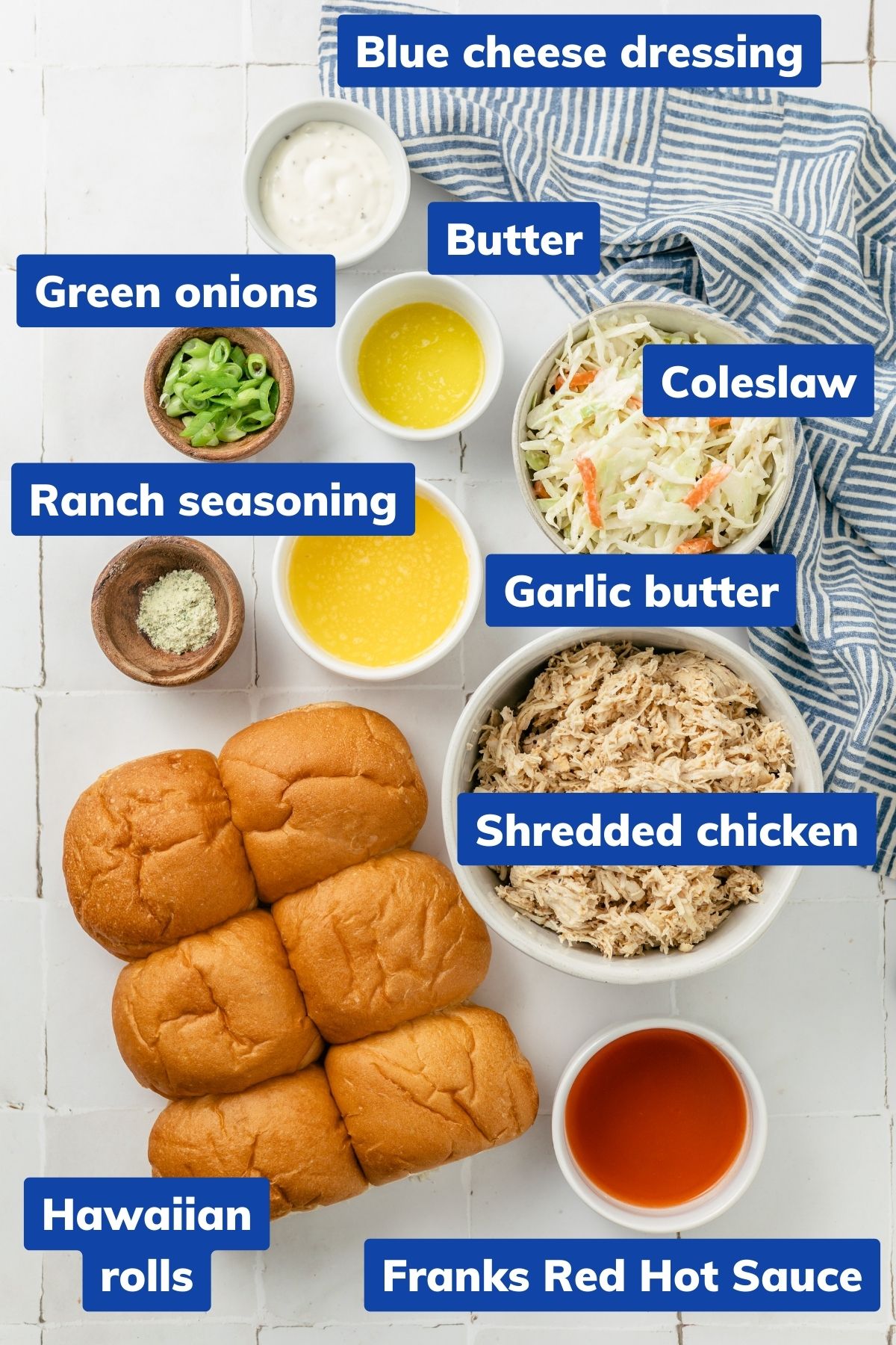 Bowls of ingredients for sliders: Sweet rolls, garlic butter, shredded chicken, ranch seasoning, hot sauce, melted butter, coleslaw, blue cheese dressing, and green onions