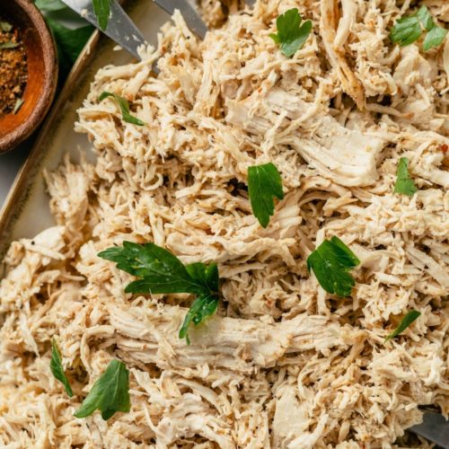 Tender and flavorful shredded chicken cooked in a pressure cooker on a plate with fresh parsley