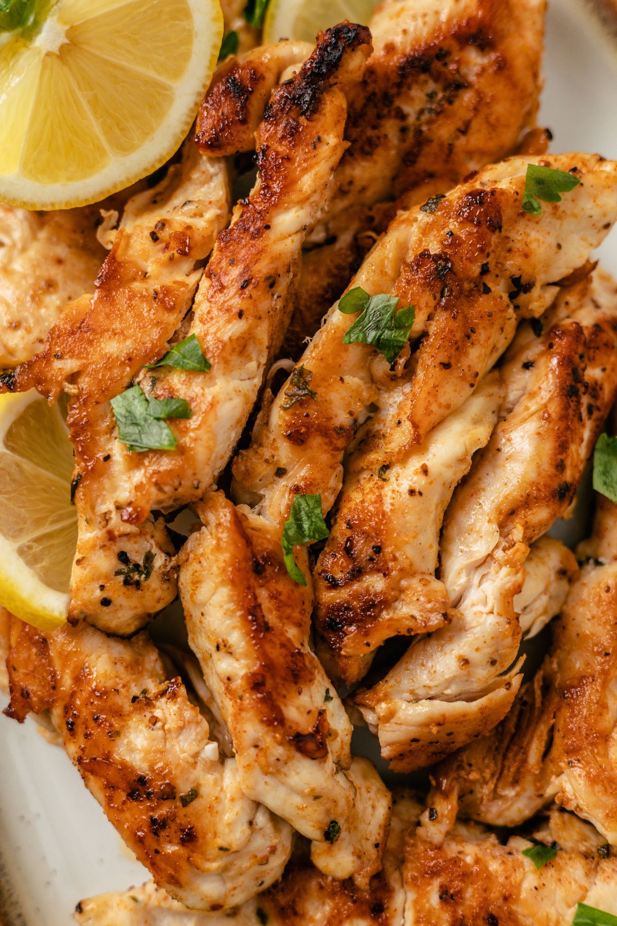 Pan-fried chicken tenders without breading, garnished with lemon slices.