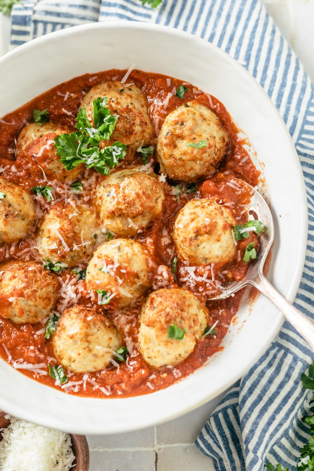 Juicy air fryer chicken meatballs in a large bowl with marinara sauce, chopped parsley and parmesan cheese.