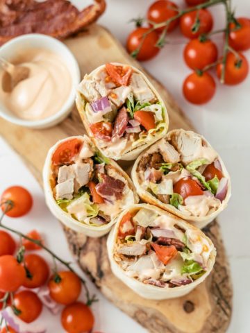 Four savory Cajun Chicken Wraps with a side of spicy mayo dip, surrounded by vibrant cherry tomatoes.