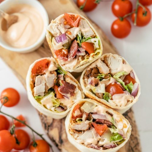 Four savory Cajun Chicken Wraps with a side of spicy mayo dip, surrounded by vibrant cherry tomatoes.