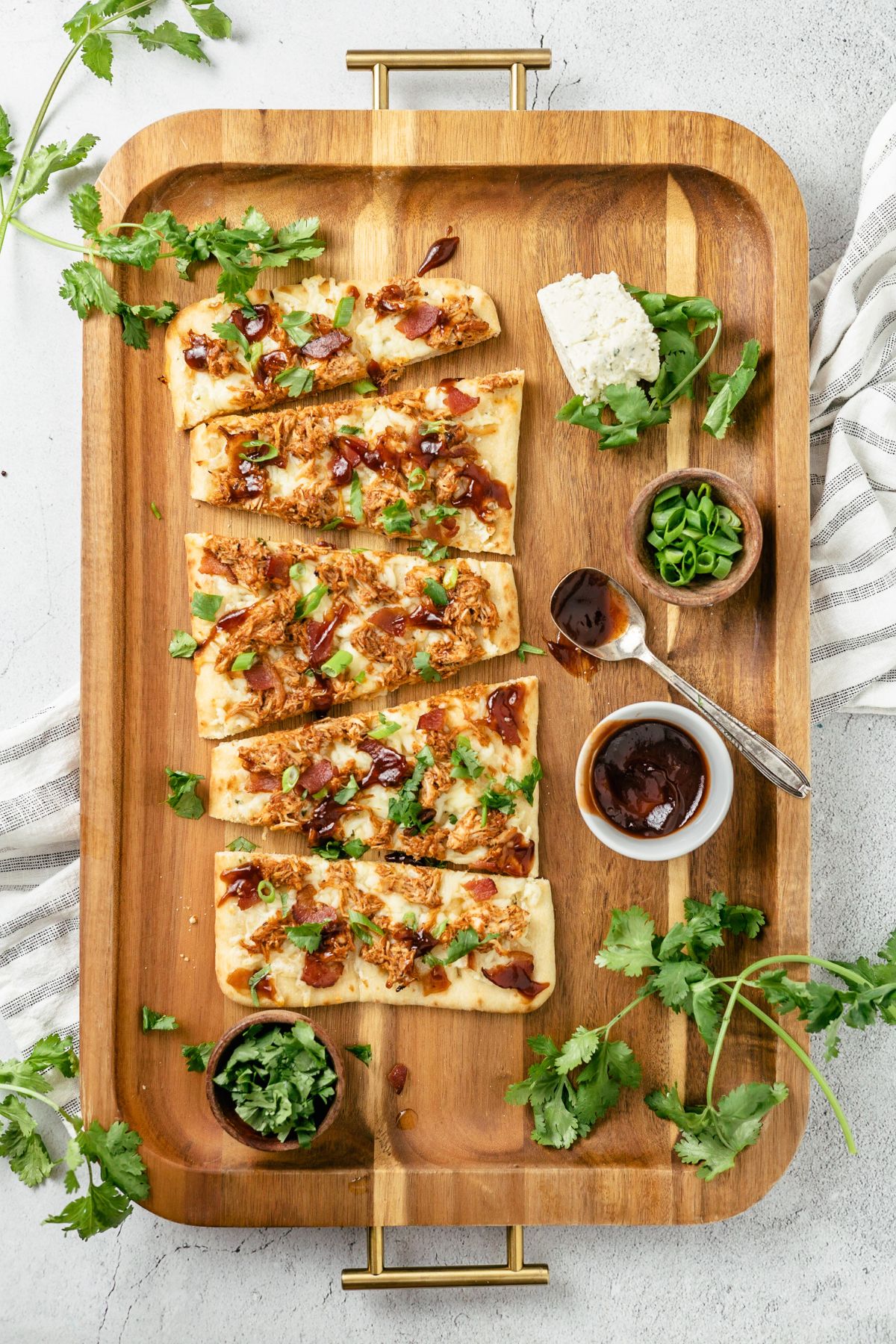 BBQ Chicken Flatbreads artistically arranged on a rustic wooden board, featuring shredded chicken, BBQ seasoning, sauce, flatbread, cheeses, green onions, bacon bits, and fresh cilantro, presenting a delightful culinary masterpiece.