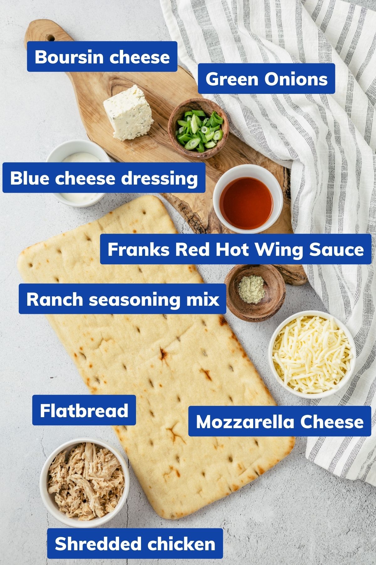 A spread of ingredients in separate bowls: Shredded Chicken, Ranch seasoning mix (garlic powder, onion powder, and more), Franks red hot wing sauce, Flatbread, Boursin cheese, Mozzarella cheese (shredded), Blue cheese dressing (homemade dip), and Green onions.