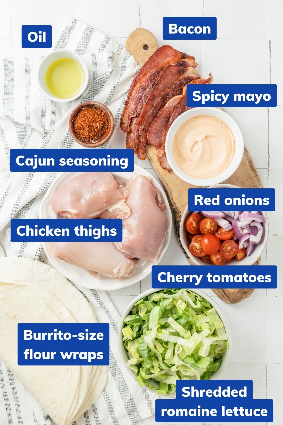 Ingredients for a delicious meal: Chicken thighs, Cajun seasoning, oil, spicy mayo, burrito-size flour wraps, shredded romaine lettuce, halved cherry tomatoes, thinly sliced red onions, and crispy bacon – all in separate bowls or containers