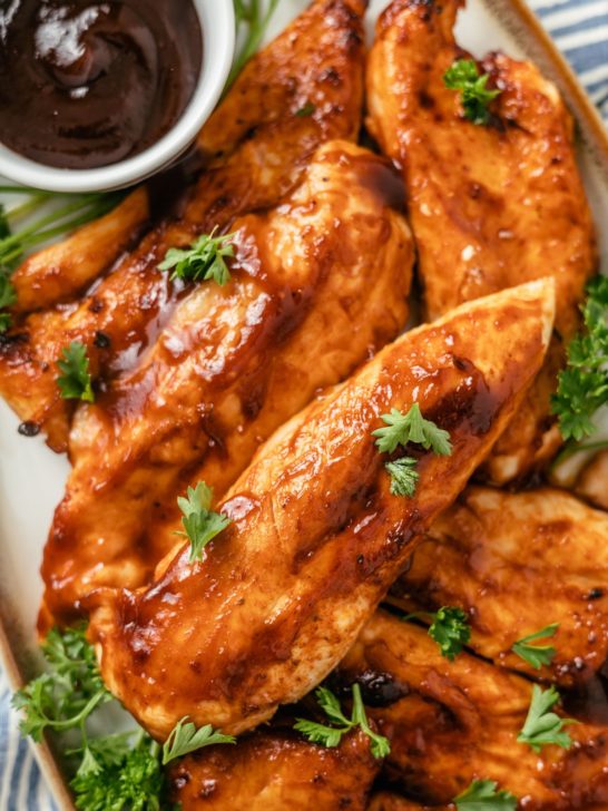 BBQ chicken tenders, adorned with fresh parsley, served on a plate with a side of flavorful BBQ sauce