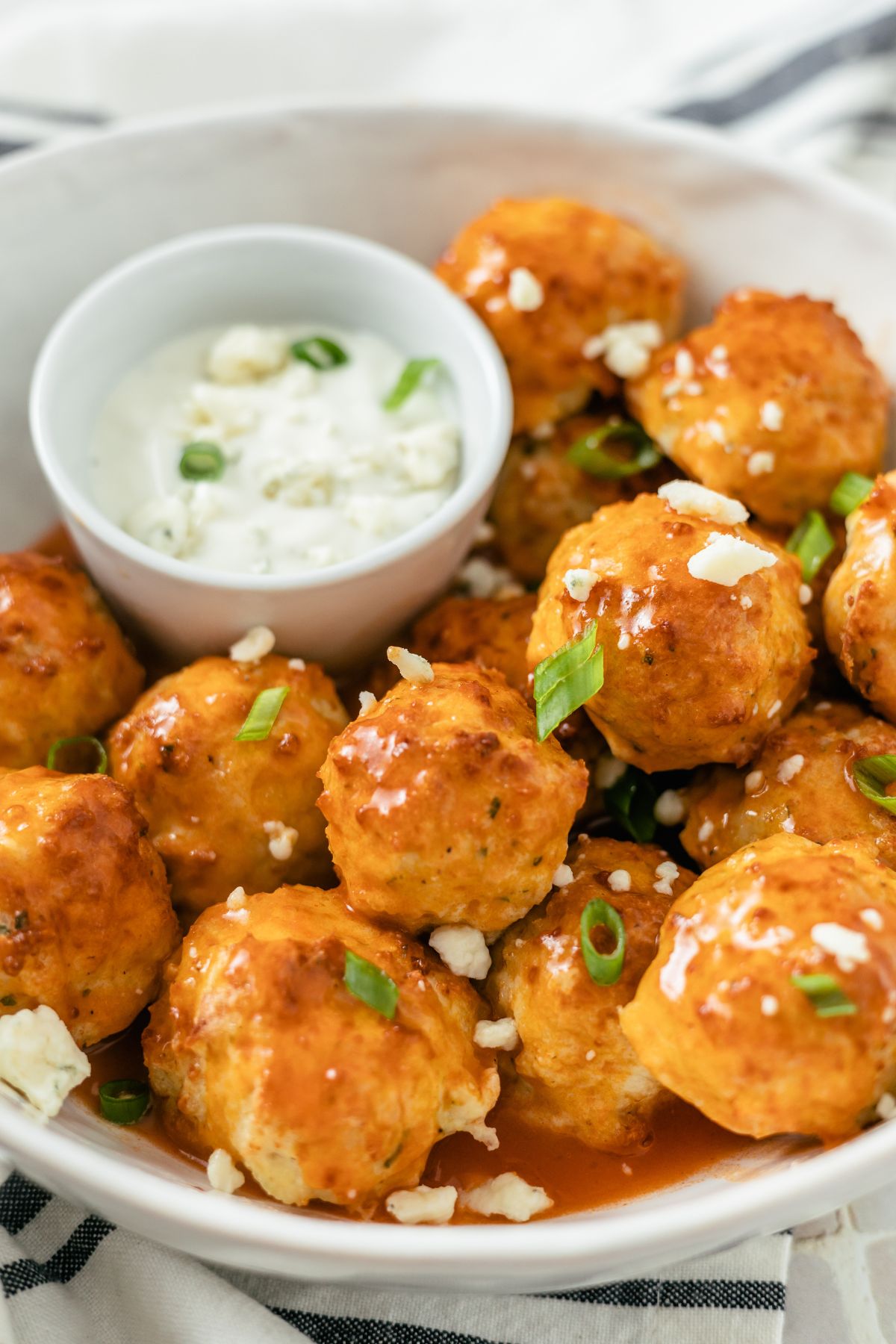 Crispy golden Buffalo Chicken Meatballs with a tender interior in a bowl with blue cheese crumbles, ranch dressing, and extra buffalo sauce.