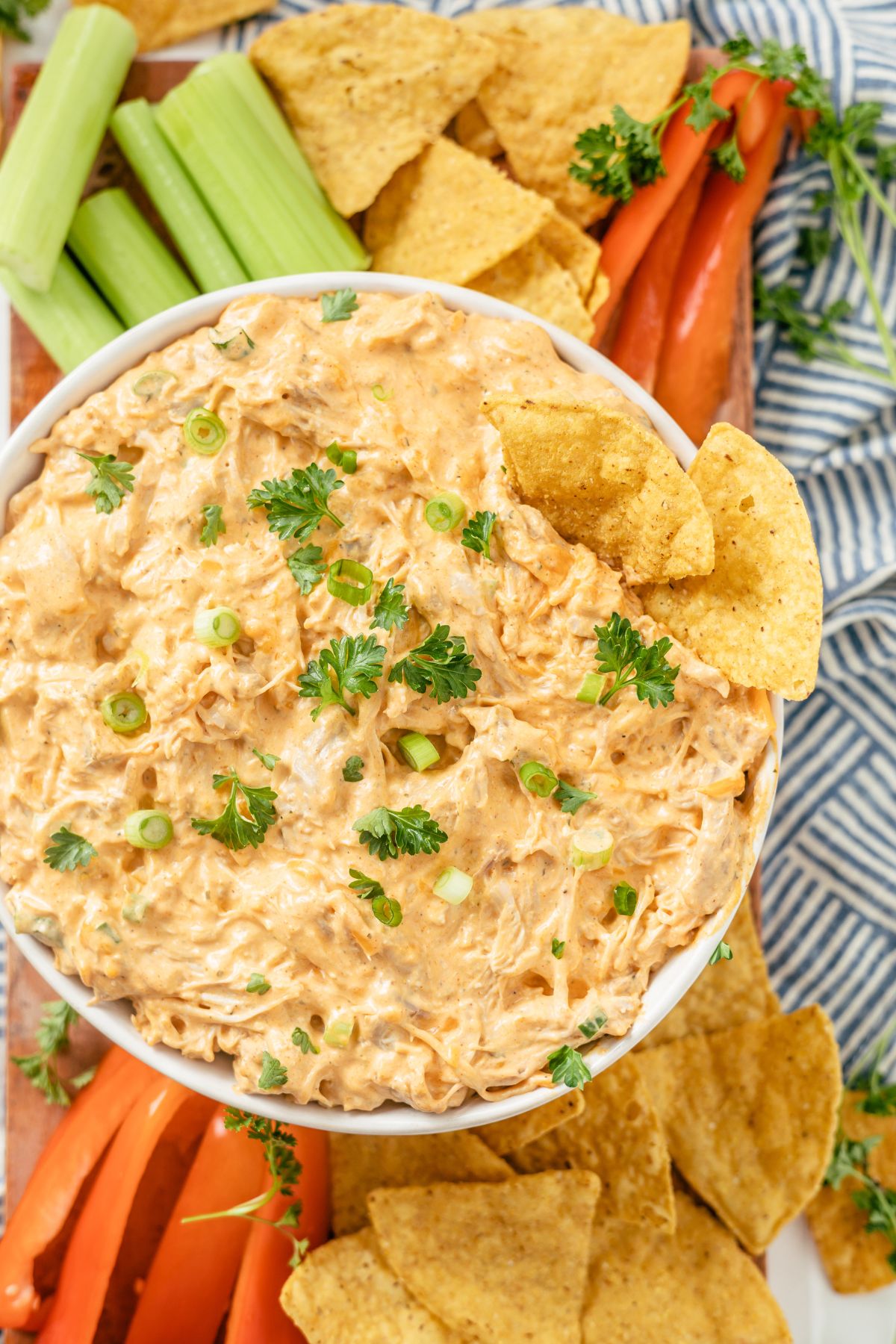 Buffalo Chicken Dip topped with parsley and green onions, surrounded by crispy chips, carrots, and celery for a tempting snack platter