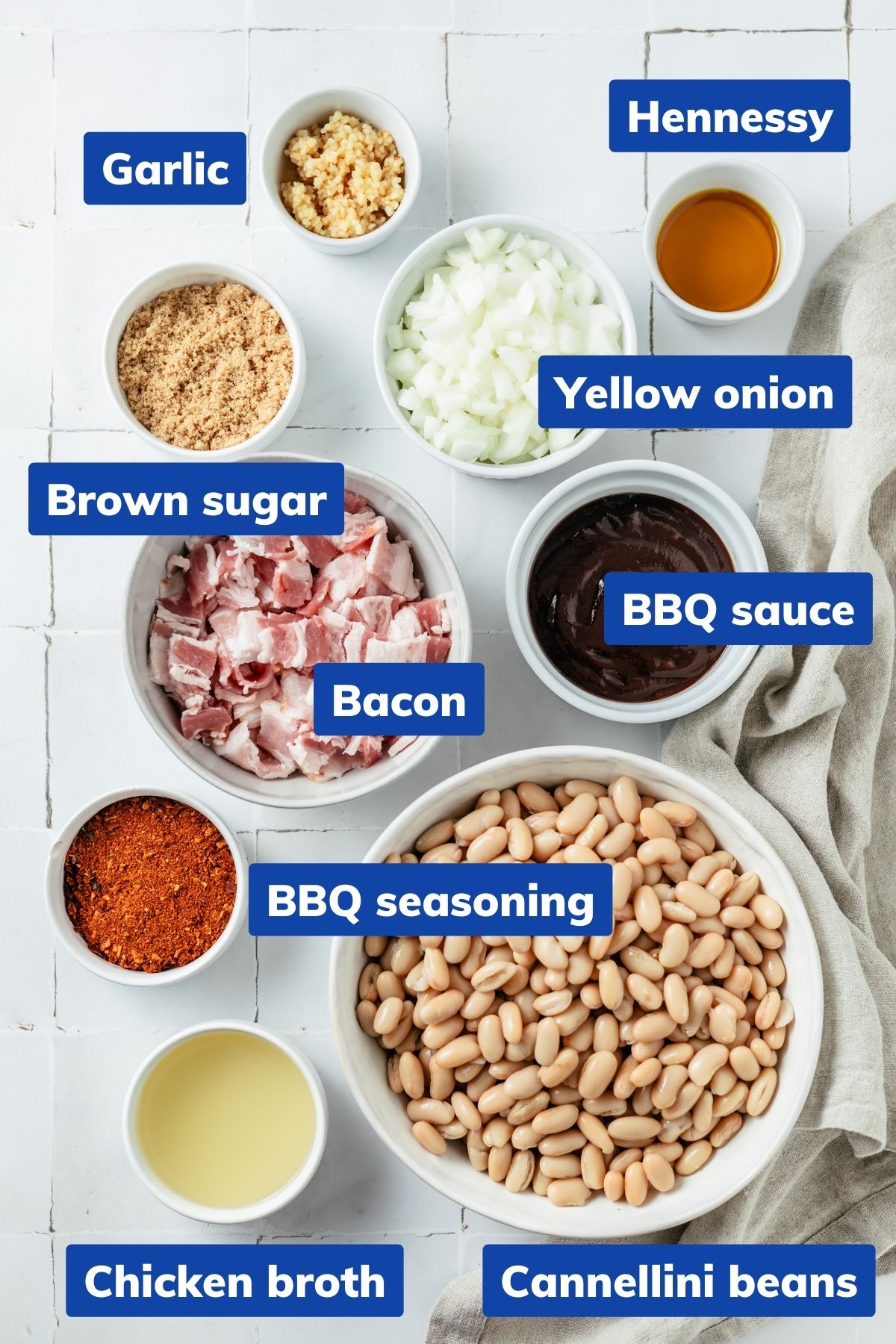 Key ingredients for Slow Cooker Baked Beans artfully displayed in separate bowls: bacon strips, diced yellow onion, minced garlic cloves, cannellini beans, low-sodium chicken broth, BBQ seasoning, hickory or Kansas City style BBQ sauce, brown sugar, and a touch of Hennessy for a flavorful touch