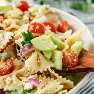 Wooden spoon scooping delicious Bowtie Pasta Salad from a large bowl.