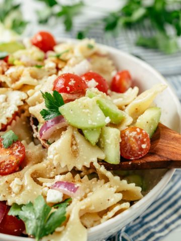 Wooden spoon scooping delicious Bowtie Pasta Salad from a large bowl.