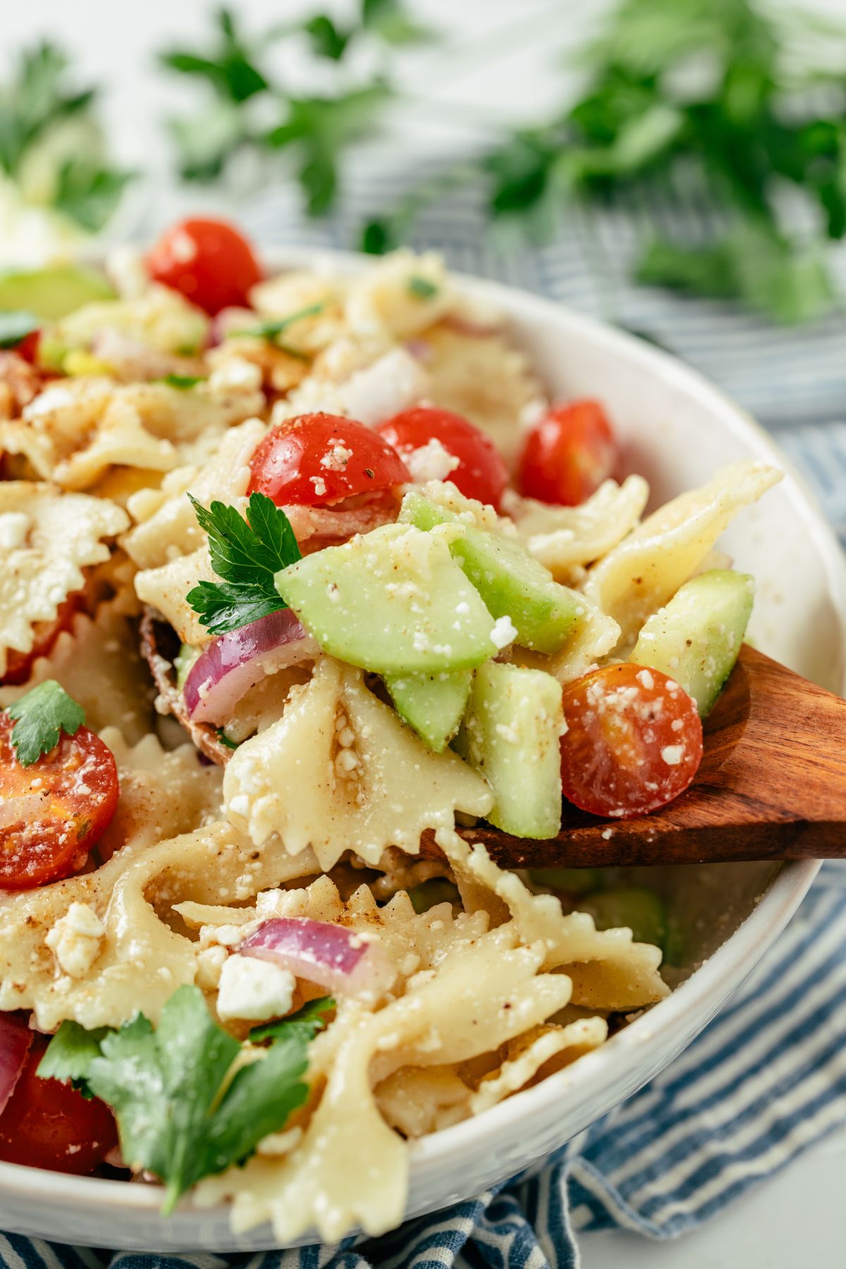 Wooden spoon scooping delicious Bowtie Pasta Salad from a large bowl.