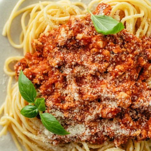 Plate of hearty ground chicken spaghetti, generously topped with marinara sauce and fresh herbs
