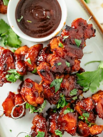 juicy baked chicken skewers with a side of BBQ sauce, presented on a white platter