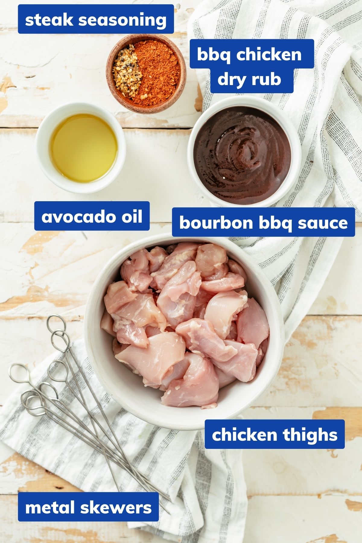 Ingredients for baked chicken skewers in separate bowls: chicken thighs, steak seasoning, BBQ dry rub, avocado oil, and bourbon BBQ sauce for Baked Chicken Skewers