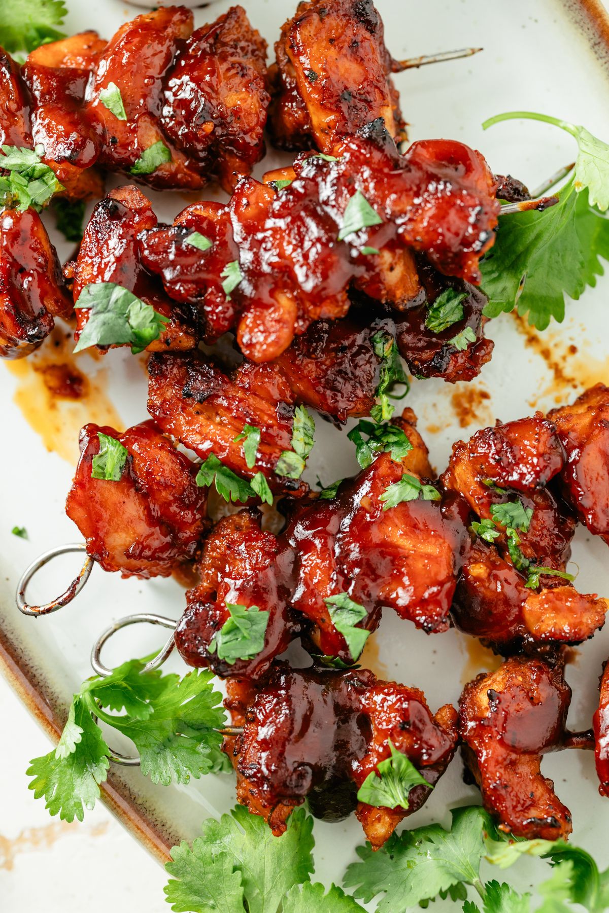 Close-up of succulent baked chicken skewers, glistening with juices and herbs on a white platter