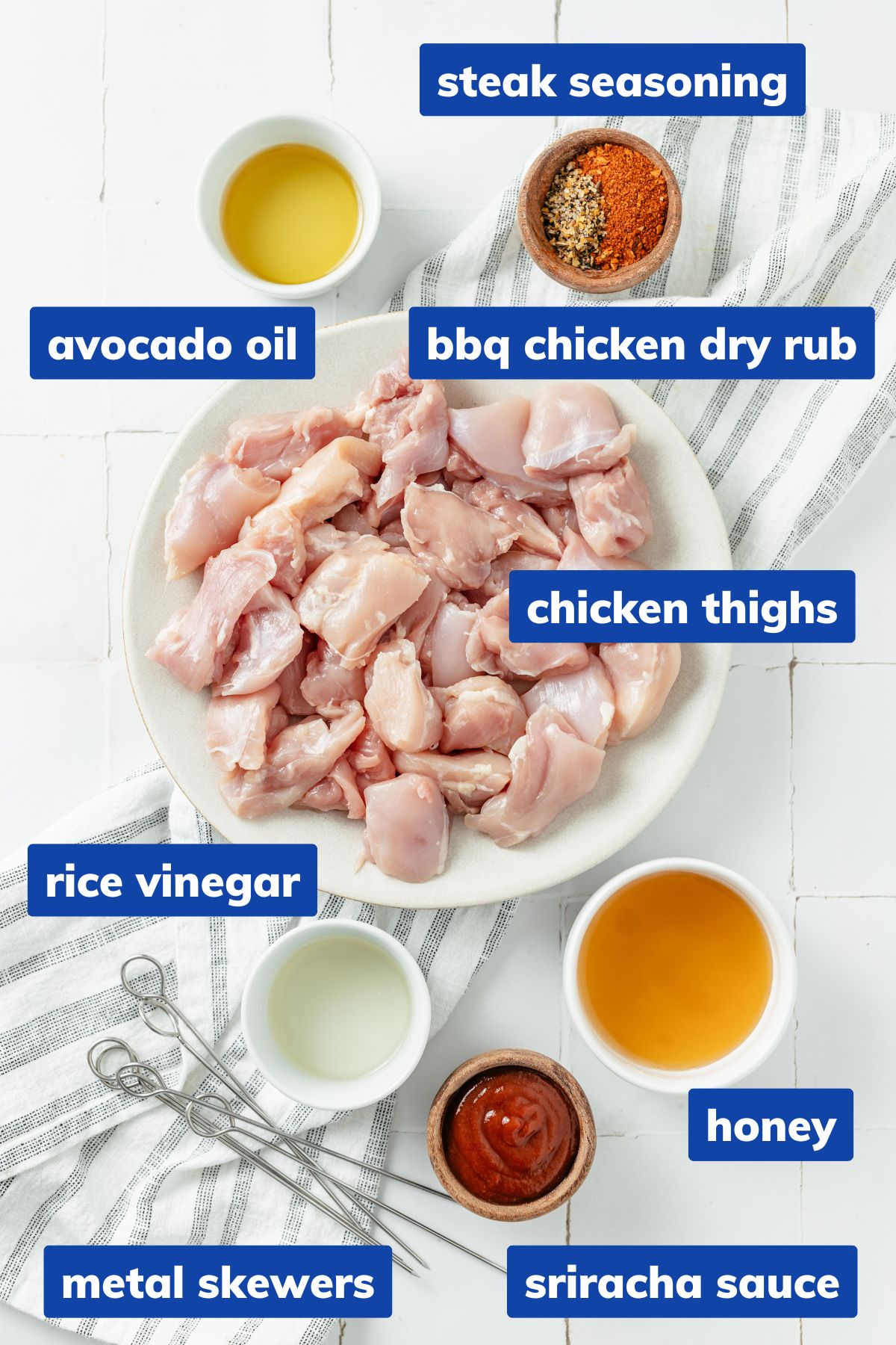 Ingredients for hot honey chicken skewers arranged in separate bowls: diced chicken thighs, steak seasoning, BBQ chicken dry rub, avocado oil, honey, sriracha sauce, and rice vinegar.