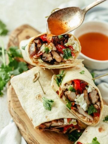 Jerk chicken wrap topped with extra sauce, filled with chicken, fresh veggies, and wrapped in a soft tortilla, ready to enjoy.
