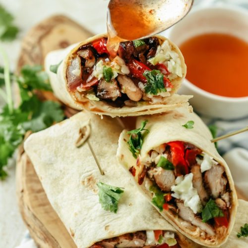 Jerk chicken wrap topped with extra sauce, filled with chicken, fresh veggies, and wrapped in a soft tortilla, ready to enjoy.