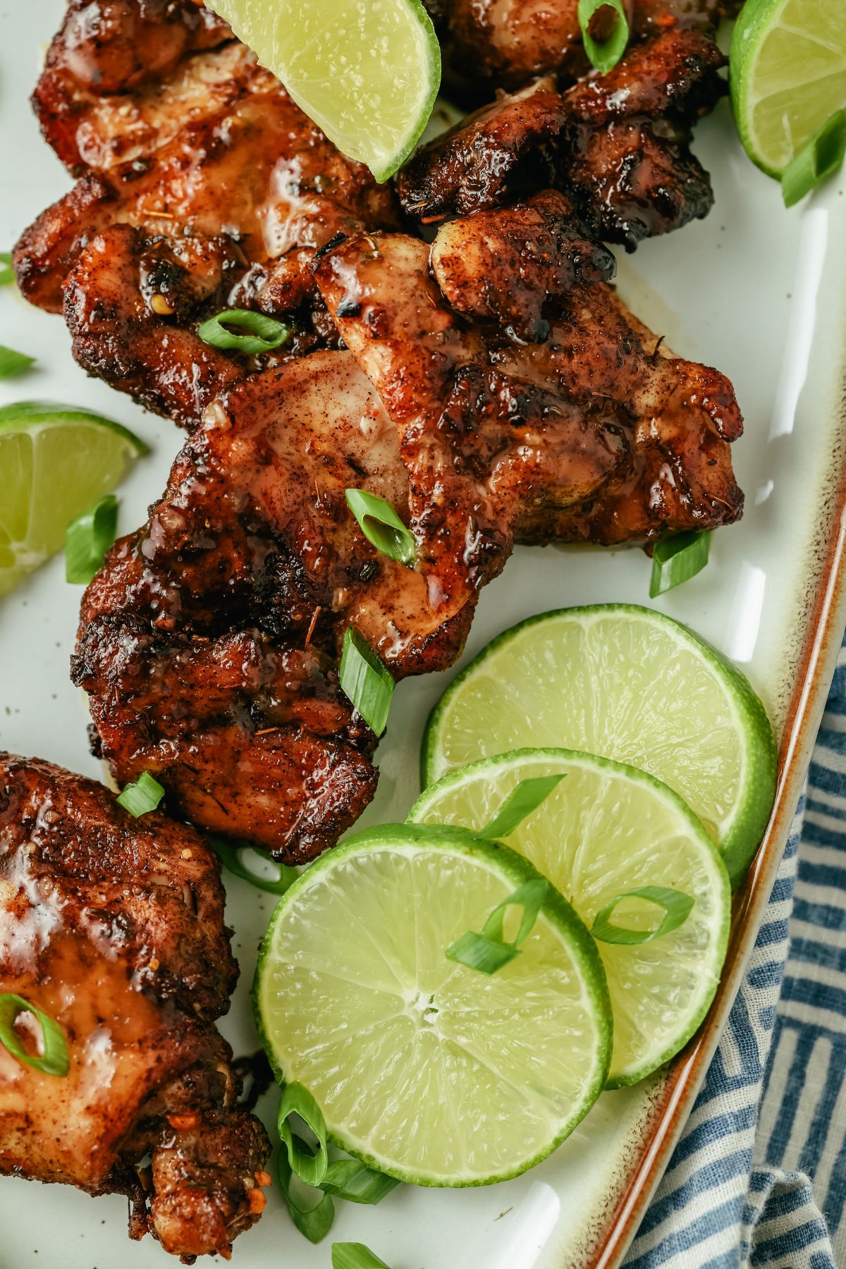 Air-fried jerk chicken thighs, richly seasoned and golden, surrounded by fresh lime slices for a burst of color and zest, beautifully arranged on a serving plate