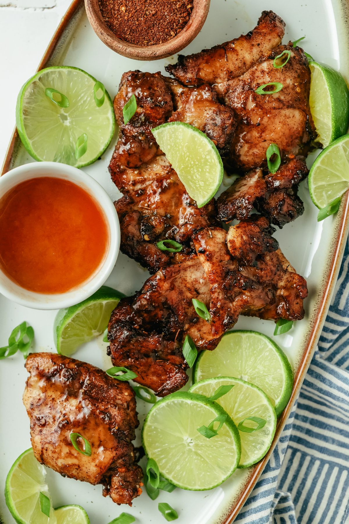 Juicy jerk chicken thighs, perfectly seasoned, surrounded by fresh lime slices, with a side of Sriracha and spicy jerk seasoning for added flavor