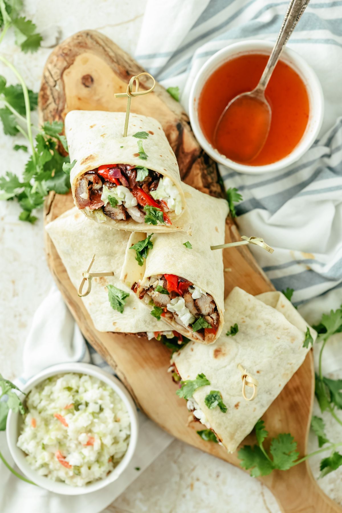 Jerk chicken wrap filled with chicken and veggies served on a wooden board with a side bowl of creamy coleslaw and extra sauce.