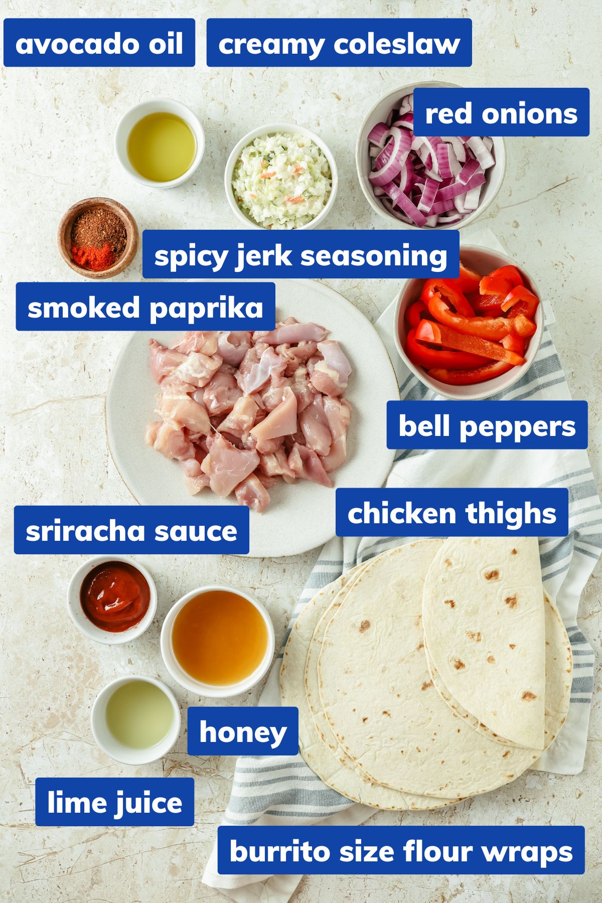 Ingredients for a jerk chicken wrap, arranged in separate bowls: bite-sized chicken thigh pieces, spicy jerk seasoning, smoked paprika, sliced bell peppers, red onion strips, avocado oil, flour wraps, sweet & spicy sauce, honey, Sriracha, lime juice, and a creamy coleslaw.