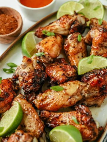 Flavorful jerk chicken wings, golden-brown and crispy, surrounded by fresh lime slices, with a small dish of Sriracha sauce for an extra kick